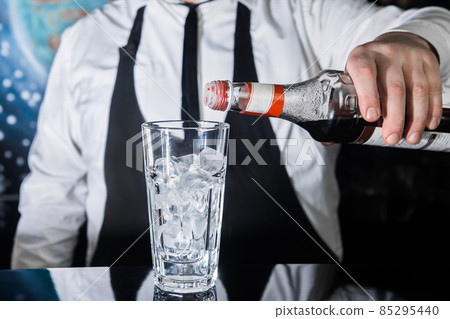 The hand of a professional bartender pours red syrup into a glass of ice cubes. The process of preparing an alcoholic cocktail 85295440