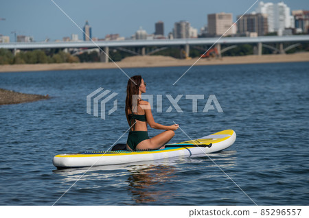 Caucasian woman is riding a SUP board on the river in the city. Summer sport. 85296557