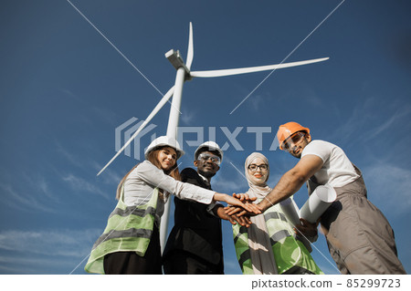 Multicultural partners stacking hands among windmill farm Multicultural partners stacking hands among windmill farm 85299723