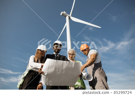 Four partners in helmets studying wind turbine blueprints Four partners in helmets studying wind turbine blueprints 85299724