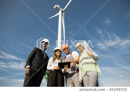 Multiracial coworkers having meeting on farm with windmills Multiracial coworkers having meeting on farm with windmills 85299729