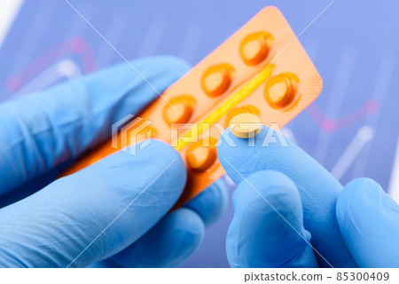 Scientist hold small pill on fingertip of one hand and blister pack in other 85300409