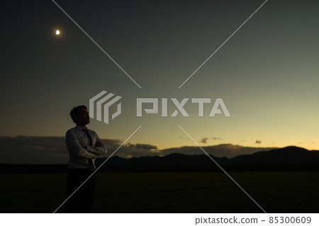 Businessman at sunset standing outdoors with folded arms Businessman at sunset standing outdoors with folded arms 85300609
