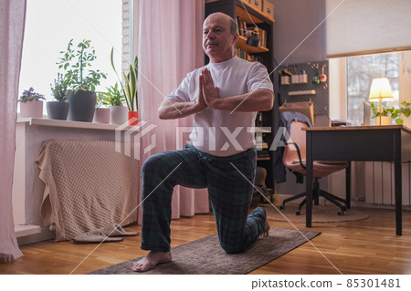 Senior hispanic man standing in warrior two yoga pose practicing in living room Senior hispanic man standing in warrior two yoga pose practicing in living room 85301481