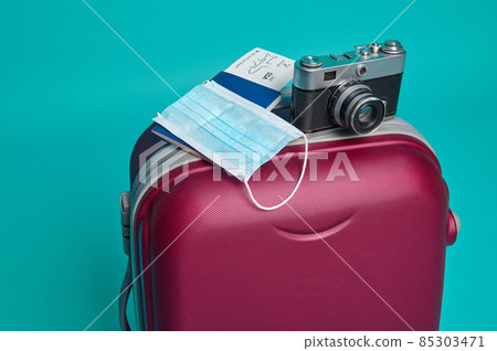 Studio shot of a suitcase, vintage camera, passport with air ticket and boarding pass, medical mask isolated over blue background with copy ad space. Tourism and travel concept 85303471