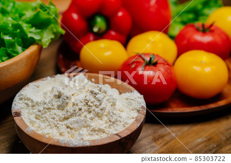 a wooden bowl of flour and vegetables on the kitchen table. farm products 85303722