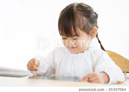 A 2-year-old girl looking at a tablet in the dining room at home A 2-year-old girl looking at a tablet in the dining room at home 85307064