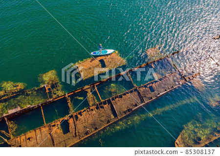 Woman on paddle board, sup next to Abandoned broken shipwreck sticking out of the sea 85308137