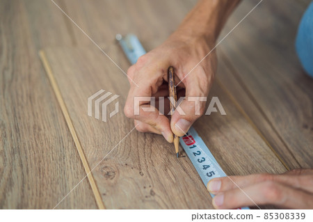Man installing new wooden laminate flooring on a warm film floor. Infrared floor heating system under laminate floor 85308339
