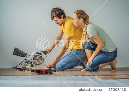 Married couple installing new wooden laminate flooring on a warm film floor. Infrared floor heating system under laminate floor Married couple installing new wooden laminate flooring on a warm film floor. Infrared floor heating system under laminate floor 85308418