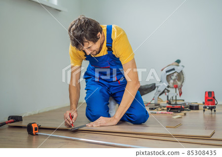 Man installing new wooden laminate flooring on a warm film floor. Infrared floor heating system under laminate floor Man installing new wooden laminate flooring on a warm film floor. Infrared floor heating system under laminate floor 85308435