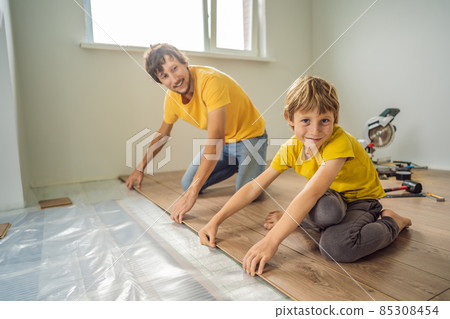 Father and son installing new wooden laminate flooring on a warm film floor. Infrared floor heating system under laminate floor 85308454