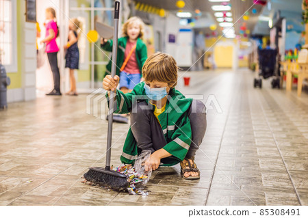 A boy in a working uniform and a medical mask sweeps the floor. Coronovirus COVID 19 concept 85308491