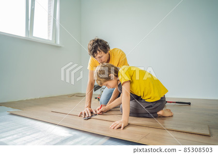 Father and son installing new wooden laminate flooring on a warm film floor. Infrared floor heating system under laminate floor 85308503