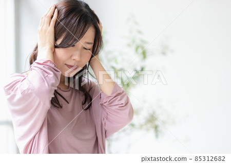 A sick woman wearing a loungewear and holding her head 85312682