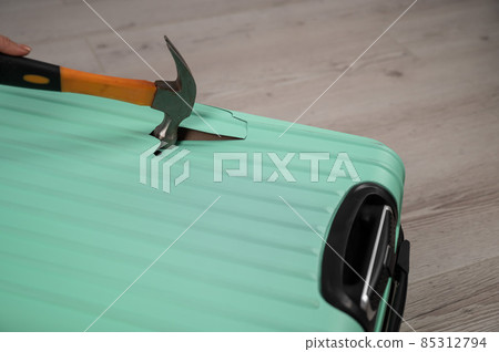A woman hits a suitcase with a hammer on a white background. 85312794