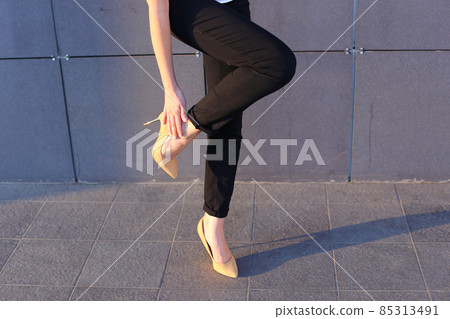 Girl holds leg rotated in profile at camera against background of wall of business center. Girl holds leg rotated in profile at camera against background of wall of business center. 85313491