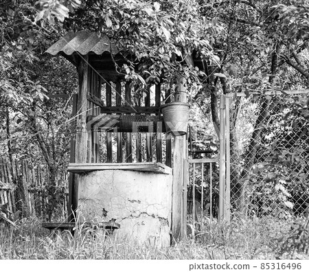 Old well with iron bucket on long forged chain for clean drinking water 85316496