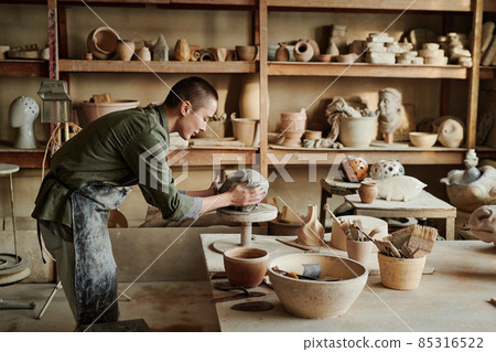 Female sculptor using equipment she holding clay with hands and making form of vase Female sculptor using equipment she holding clay with hands and making form of vase 85316522