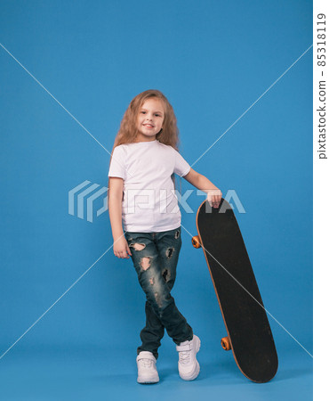 A stylish little girl is learning to skateboard on an isolated blue background. 85318119