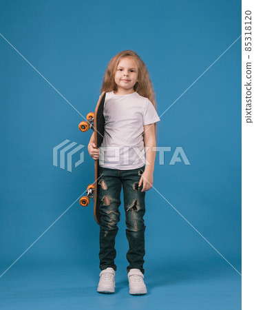 A stylish little girl is learning to skateboard on an isolated blue background. 85318120