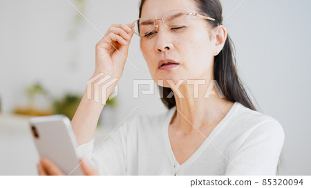 Senior woman looking into a smartphone with reading glasses 85320094