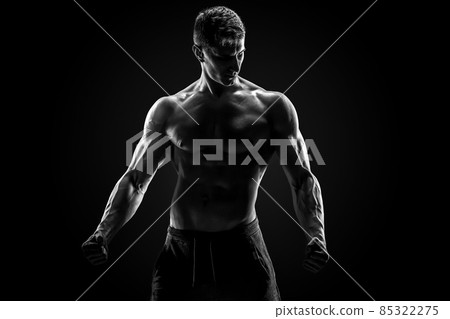 Sexy muscular man posing with naked torso on black background Sexy muscular man posing with naked torso on black background 85322275