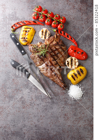 Beef T-Bone steak with grilled vegetables and seasoning on grey background. Vertical top view Beef T-Bone steak with grilled vegetables and seasoning on grey background. Vertical top view 85322418