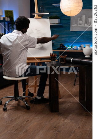 Man painter sitting in front of canvas drawing vase 85326262