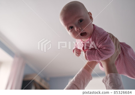 Portrait of caucasian mother lifting and playing with newborn baby, baby talking to mother. 85326684