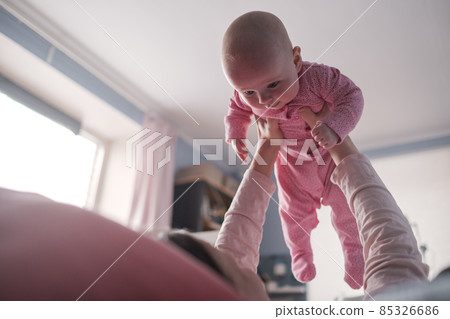 Portrait of caucasian mother lifting and playing with newborn baby, baby talking to mother. 85326686