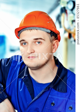 Portrait of young engineer in helmet in working environment at factory. Gas worker confidently looks Portrait of young engineer in helmet in working environment at factory. Gas worker confidently looks 85327661