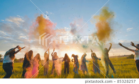 Cheerful girls toss up multi-colored powder at a beautiful sunset. 85328257