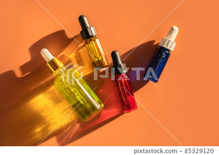 Transparent glass dropper bottles with green, red and blue liquid inside on orange beige background in the sunlight. Pipette with fluid hyaluronic acid, serum, retinol. Cosmetics, healthcare, beauty Transparent glass dropper bottles with green, red and blue liquid inside on orange beige background in the sunlight. Pipette with fluid hyaluronic acid, serum, retinol. Cosmetics, healthcare, beauty 85329120