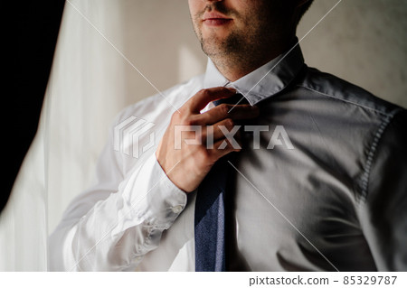men's hands tie a tie around their neck over a white shirt. men's hands tie a tie around their neck over a white shirt. 85329787
