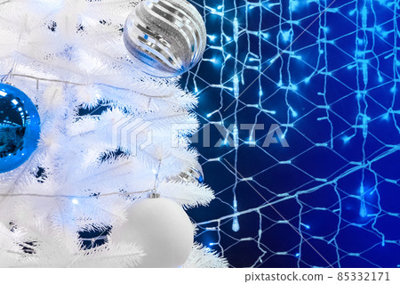 White artificial Christmas tree decorated with balls against the background of blue Christmas lights White artificial Christmas tree decorated with balls against the background of blue Christmas lights 85332171