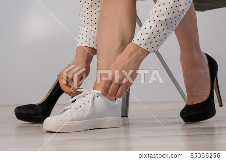 Close-up business woman takes off her shoes puts on white leather sneakers. 85336256