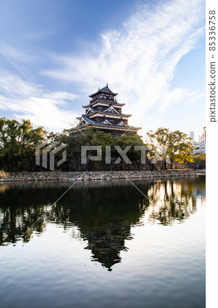 It is the castle tower of Hiroshima Castle and the scenery of the central park. There is a shadow on the surface of the moat. 85336758