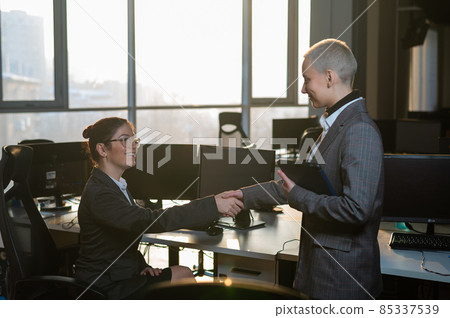 Two young business women shake hands at work. The office staff made a deal Two young business women shake hands at work. The office staff made a deal 85337539