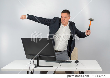 The man gets angry and smashes the monitor with a hammer. An office worker in a rage breaks the computer. The man gets angry and smashes the monitor with a hammer. An office worker in a rage breaks the computer. 85337540