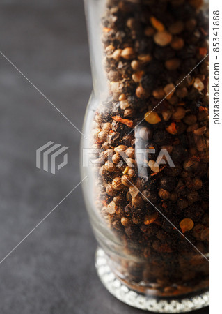 A mixture of seasonings, spices and herbs in a glass mill on a black background. A mixture of seasonings, spices and herbs in a glass mill on a black background. 85341888
