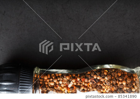 A mixture of seasonings, spices and herbs in a glass mill on a black background. 85341890