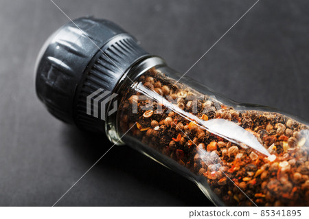 A mixture of seasonings, spices and herbs in a glass mill on a black background. 85341895