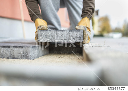 Man laying a paving brick placing it on the sand foundation Man laying a paving brick placing it on the sand foundation 85343877