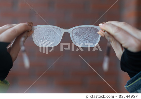 A woman holds frozen glasses covered with frost on the background of a brick wall 85344957