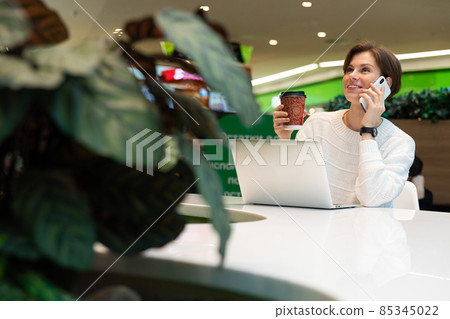 Young beautiful smiling woman sitting at a shopping center at a table and working at a computer 85345022