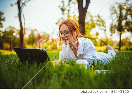 beautiful smiling girl student uses laptop pc while lying on the grass outdoors. Education concept beautiful smiling girl student uses laptop pc while lying on the grass outdoors. Education concept 85345500