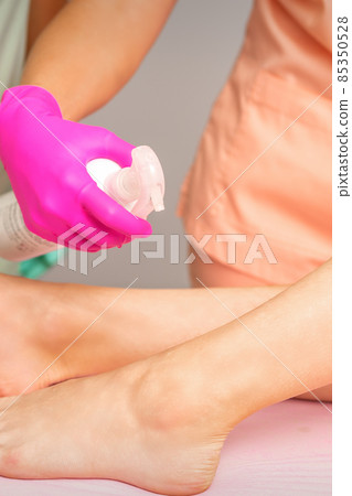A beautician sprays a disinfectant on the feet of a young woman before the epilation procedure. Foot depilation. A beautician sprays a disinfectant on the feet of a young woman before the epilation procedure. Foot depilation. 85350528