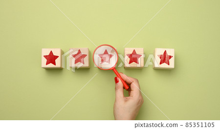 five red stars and a hand with a plastic magnifier on a green background. Evaluation of the quality of services and goods, high rating 85351105