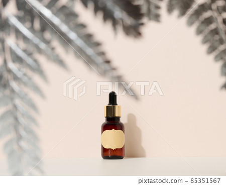 brown glass bottle with a pipette stands on a brown background. Container for cosmetics, serum and oil, silver fern leaf 85351567